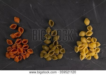 Top View Of Dry Conchiglie Pasta On Black Board Background. Three Triangular Slides With Pasta Conch