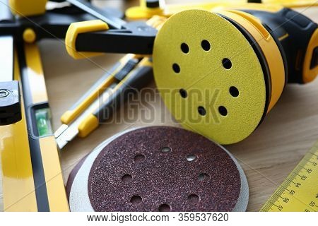 Close-up Of Bright Yellow Sander Machine And Replacement Discs On Wooden Table. Carpenters Essential