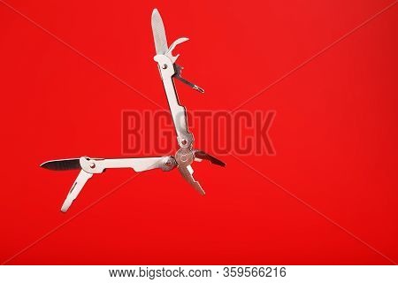 Multitool Is A Multi-functional Tool On A Red Background. The Concept Of An Open, Flying Multi-tool 