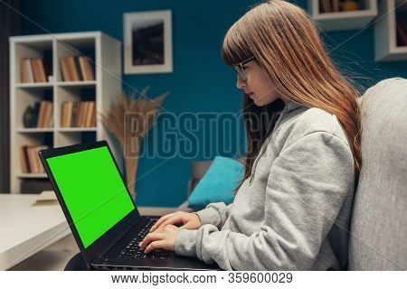 Side View Of Little Girl Sitting On Sofa With Portable Computer On Lap Typing Keyboard, Chromakey Sc