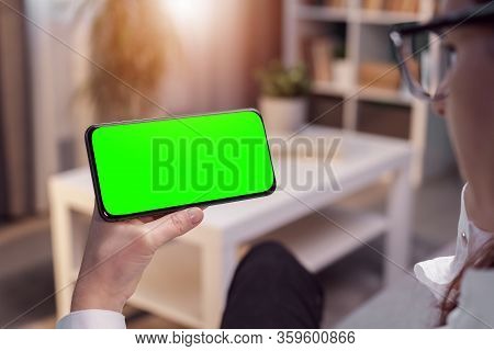 Person Horizontally Holding Smartphone With Green Screen Sitting In Flat, Sunlit Window