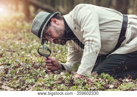 Half-body Pic Of Presentable-looking Man Studying Vegetation Through Loupe Kneeling On Ground In Par