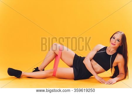 Athletic Girl Performs Exercises Using A Resistance Band. Photo Of Young Girl On Drey Background. St
