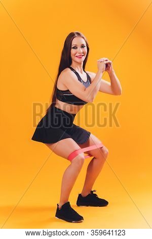 Athletic Girl Performs Exercises Using A Resistance Band. Photo Of Young Girl On Drey Background. St