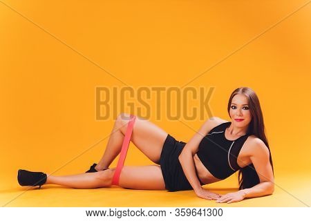 Athletic Girl Performs Exercises Using A Resistance Band. Photo Of Young Girl On Drey Background. St