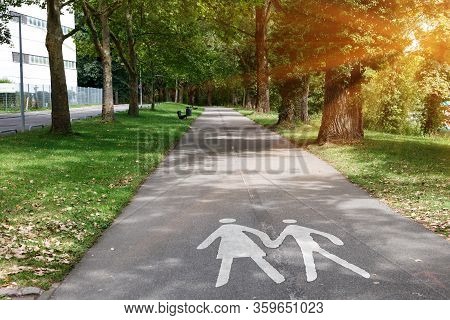 Two Silhouettes Of Man And Woman On An Empty Footpath In The Park On A Sunny Day. Sign Pedestrians O
