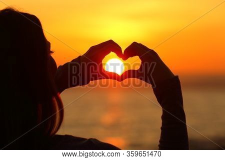 Close Up Of A Girl Hands Silhouette Making Heart Shape Arround The Sun At Sunset On The Beach
