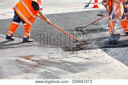 The Working Team Smoothes Hot Asphalt With A Metal Levels And Shovels By Hand When Repairing The Roa