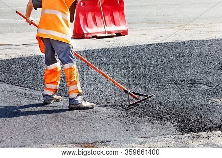 A Road Service Worker Updates A Stretch Of Road With Fresh Hot Asphalt And Smoothes It With A Metal 