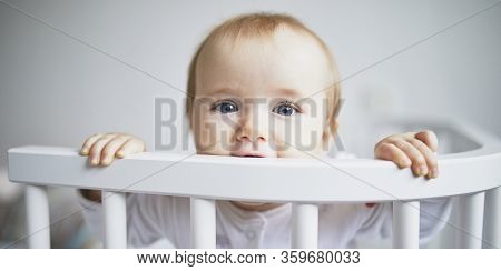 Adorable Baby Girl In Co-sleeper Crib Attached To Parents Bed. Little Kid Sitting In Cot
