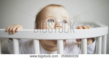 Adorable Baby Girl In Co-sleeper Crib Attached To Parents Bed. Little Kid Sitting In Cot