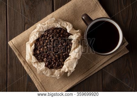 Grains Of Brown Coffee In A Paper Saucer On A Linen Napkin Next To A Cup Of Fragrant Coffee, On A Br