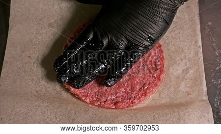 Cook Makes Meat Medallions For Burgers. Chef In Black Food Gloves Makes Cutlet. Cutlets Are Leveled 
