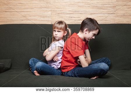 Frustrated siblings sittng on sofa stuck at home during isolation. Quarantine and lockdown protective measures against spreading of coronavirus pandemic disease