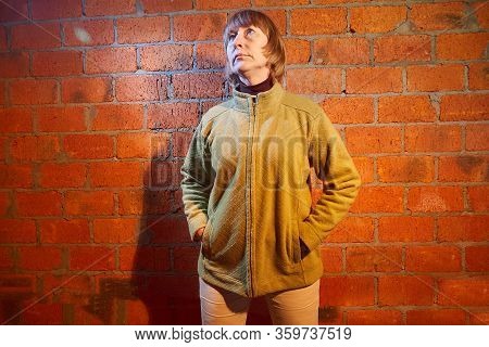 A Middle-aged Woman Poses Showing Clothes Near Red Brick Wall. An Inept Model In An Inept Shoot