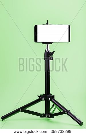 Mobile Phone On A Tripod With A Clear White Display For Images And Text, Green Isolated Background.