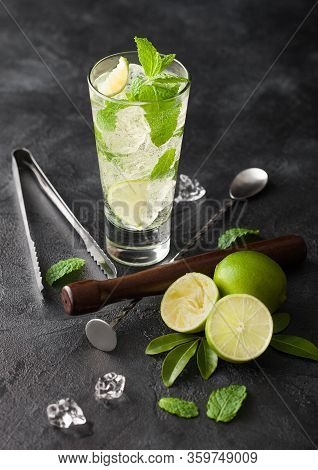 Glass Of Mojito Cocktail With Ice Cubes Mint And Lime On Black Board With Spoon And Muddler And Fres