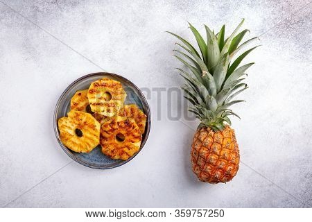 Grilled Pineapple Slices On Gray Plate And Whole Pineapple On Concrete Background. Top View. Copy Sp