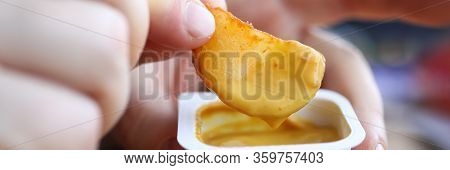 Close-up Of Persons Hand Dipping Fried Potato In Tasty Cheese Sauce. Yummy Snack For Quick Break In 