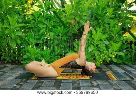 Outdoor Yoga Practice In The Garden. Young Woman Practicing Matsyasana. Fish Pose Is A Reclining Bac