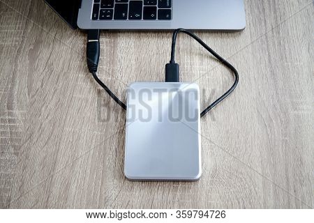 Portable Hard Drive Connected To A Laptop Computer On A Wooden Table. Data Transfer Or Backup Betwee