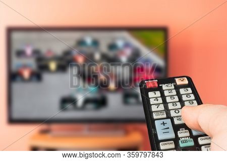 Caucasian Man Watching Formula 1 Race On Tv At Home. Changing Channels And Adjusting Volume With Tel