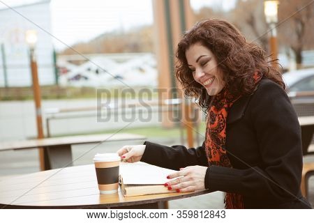 A Very Pretty Woman Laughs Merrily While Reading A Fascinating Book On The Terrace Of A Street Resta
