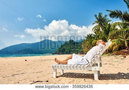 Man in white relaxing in sun bed on a tropical beach at Tioman Island, Malaysia