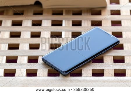 Brech/ Belgium - April 1 2020: A Portrait Of A Smartphone Lying On A Wooden Table Top With In The Ba