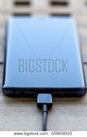 Brecht, Belgium - April 1 2020: A Portrait Of A Smartphone With A Usb Cable In Its Port. It Is Eithe