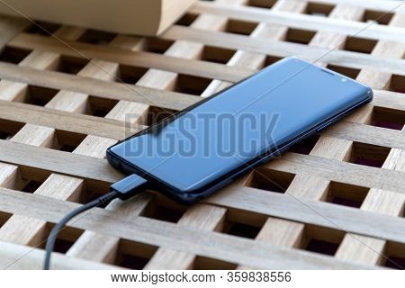 Brecht/belgium - April 1 2020: A Portrait Of A Smartphone Lying On A Table With A Usb Cable In Its P