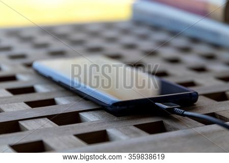 Brecht/belgium - April 1 2020: A Portrait Of A Smartphone With A Usb Cable In Its Port Lying On A Ta