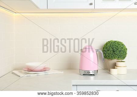 Modern Electric Kettle, Dishes And Houseplant On Counter In Kitchen