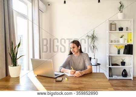 Concept Of Online Learning, Educational Webinars. A Young Woman Sits At A Table With A Laptop And Wa