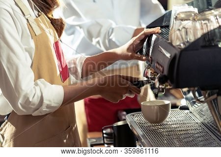 close-up shot of a barista brewing coffee by modern coffeemaker machine to making a cup of coffee with other barista working in background. Using for small business entrepreneur owner concept.