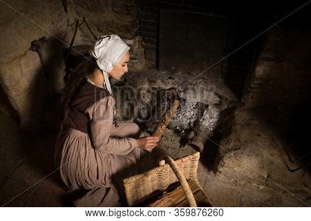 Renaissance portrait in Rembrandt style of a young woman in medieval peasant costume working near the authentic fireplace of a property released French castle