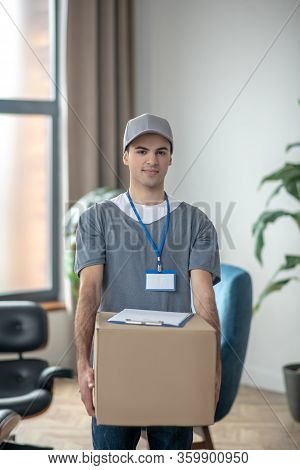 Delivery Courrier In A Cap Standing With A Big Box In His Hands