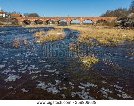 Beautiful Sunny View Of River Wenta Flowing Towards Old Brick Bridge In Old Historic Countryside Cit