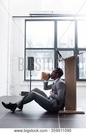 Stressed African American Speaker Breathing With Paper Bag And Having Panic Attack During Business C