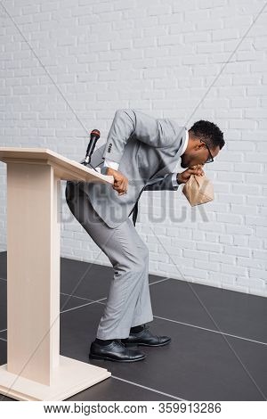 Stressed African American Speaker Breathing With Paper Bag And Having Panic Attack On Business Confe