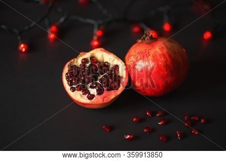 Ripe Beautiful Cut Pomegranate On A Black Background With Red Lanterns. Pomegranate Seeds Are Scatte