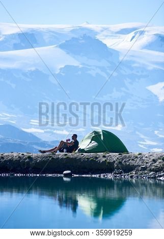 Side View Of Man Enjoying Scenery, Sitting In Chair Near Tent And Drinking Hot Tea, Admiring Fantast