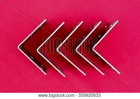 Arrow Made Of Brackets Isolated On Pink. Metal Corners Are Directed To The Left With A Place For The