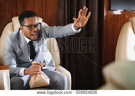 Stressed African American Businessman With Paper Bag Having Panic Attack During Flight And Showing S
