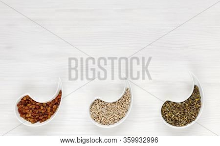 Peeled Sunflower Seeds, Pumpkins And Raisins Lie On A White Wooden Table In Beautiful Plates, Top Vi