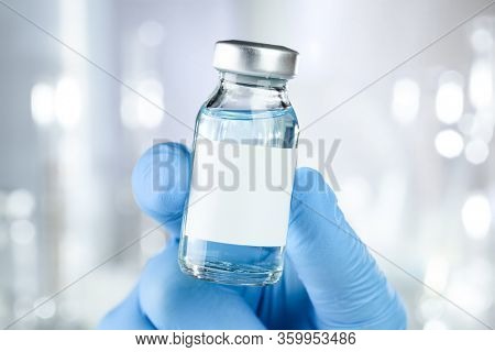 Healthcare concept with a hand in blue medical gloves holding a vaccine vial with blue liquid and black white label