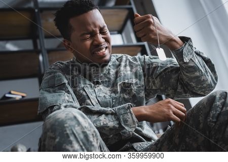 Crying African American Soldier Holding Army Badge At Home, Suffering From Ptsd