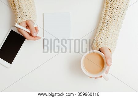 Top View A Young Girl With Her Right Hand Holding A Coffee Cup On A White Table Next To A Phone With