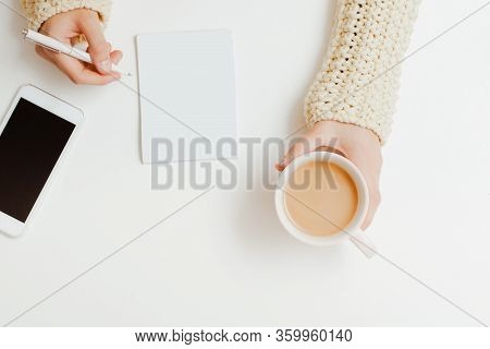 Top View A Young Girl With Her Right Hand Holding A Coffee Cup On A White Table Next To A Phone With