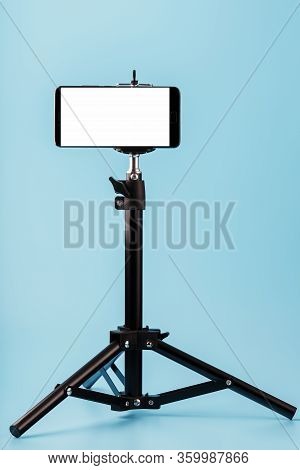 Mobile Phone Mounted On A Tripod With A White Display Free For Images And Text, Blue Isolated Backgr